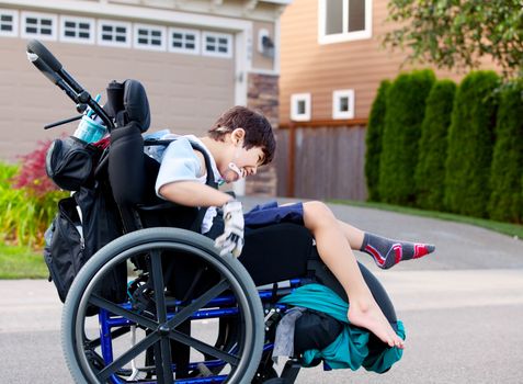 Happy little disabled boy wheeling around outdoors in wheelchair