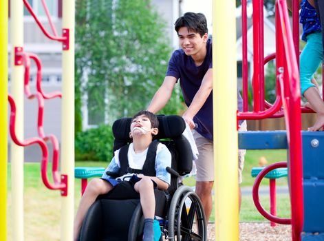 Disabled boy in wheelchair enjoying watching friends play at park on jungle gym