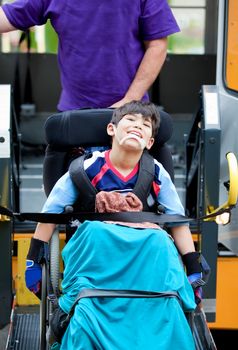 Happy disabled seven year old boy being transported on handicap school bus lift