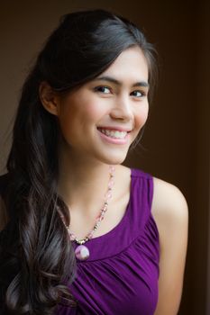 Beautiful biracial young woman in purple dress smiling , side view