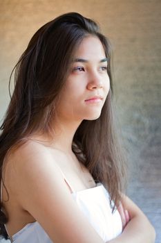 Biracial teen girl in white gown, arms crossed looking off to side