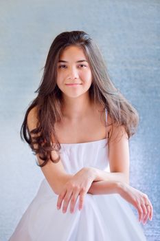Beautiful biracial teen girl in white dress, sitting arms crossed at knees