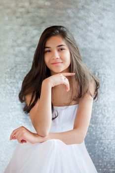 Beautiful biracial teen girl in white dress sitting, thinking towards camera
