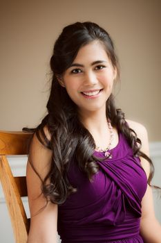 Beautiful biracial young woman in purple dress relaxing in chair