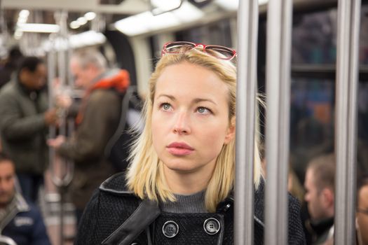 Beautiful blonde caucasian lady wearing winter coat traveling by metro in rush hour. Public transport.