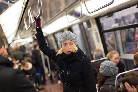 Beautiful blonde caucasian lady wearing winter coat traveling by metro in rush hour. Public transport.