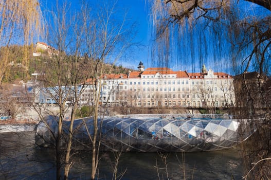 Graz, Austria - January 16, 2011: Island on Mur river connected by a modern steel and glass bridge, Styria, Graz, Austria