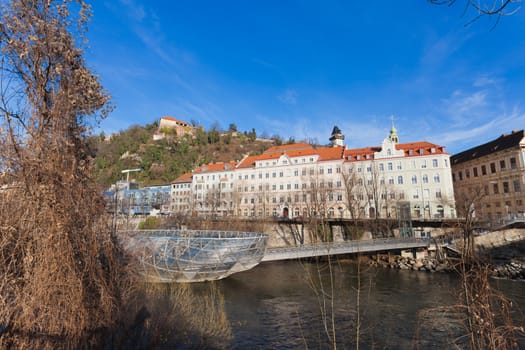 Graz, Austria - January 16, 2011: Island on Mur river connected by a modern steel and glass bridge, Styria, Graz, Austria