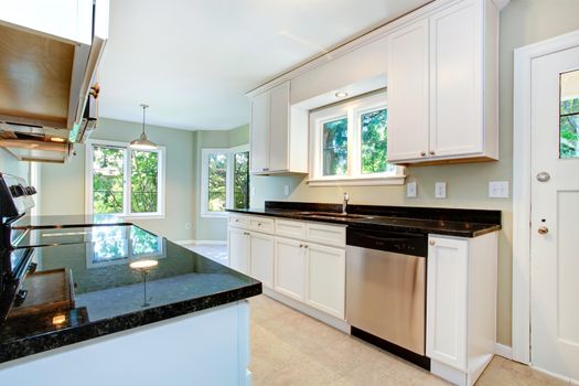 White ktichen cabinets with black granite tops and steel dish washer. Kitchen with empty dining area