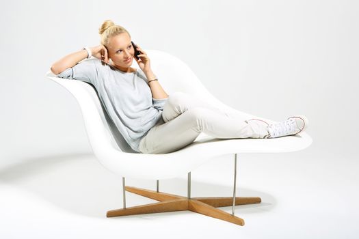 Blonde talking on mobile phone while sitting on a stylish white chair