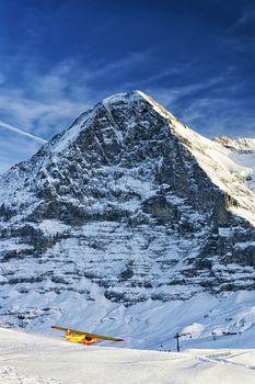 Yellow airplane taking off from alpine resort in swiss alps in winter