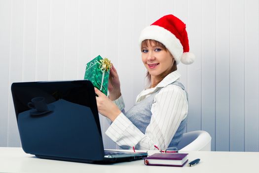 Attractive girl in the office in Santa hats with a laptop and a gift