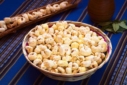 Sweetened popped white corn called Pasancalla eaten as snack in Bolivia served in a woven basket with coca tea in the back, photographed with natural light (Selective Focus, Focus on the first half of the snack) 
   