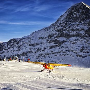 Yellow airplane landing to  alpine resort in swiss alps in winter