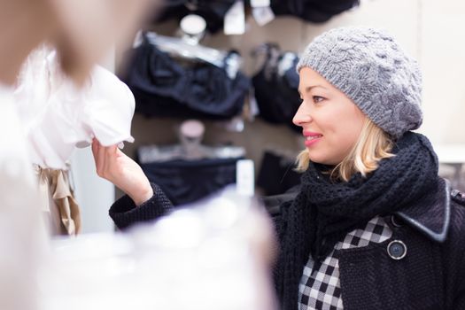 Woman shopping lingerie . Shopper looking and choosing clothing indoors in store. Beautiful blonde caucasian female model wearing winter coat and fashionable knitted cap.