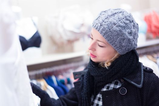 Woman shopping lingerie . Shopper looking and choosing clothing indoors in store. Beautiful blonde caucasian female model wearing winter coat and fashionable knitted cap.