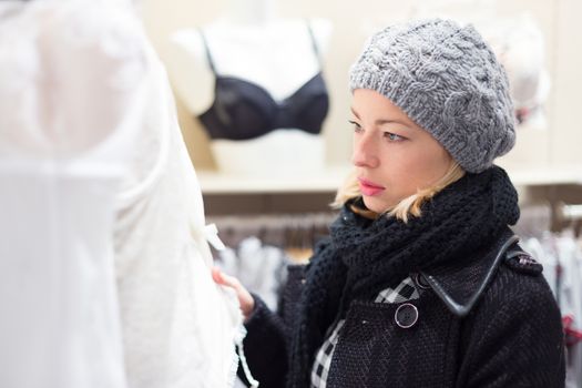 Woman shopping lingerie . Shopper looking and choosing clothing indoors in store. Beautiful blonde caucasian female model wearing winter coat and fashionable knitted cap.