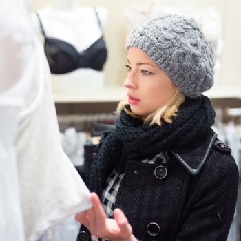 Woman shopping lingerie . Shopper looking and choosing clothing indoors in store. Beautiful blonde caucasian female model wearing winter coat and fashionable knitted cap.