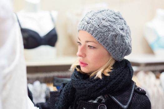 Woman shopping lingerie . Shopper looking and choosing clothing indoors in store. Beautiful blonde caucasian female model wearing winter coat and fashionable knitted cap.