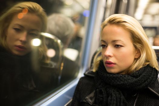 Thoughtful lady riding on a subway and looking out the window. Reflection of her face can be seen in the window.