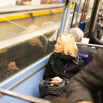 Thoughtful lady riding on a subway and looking out the window. Reflection of her face can be seen in the window.