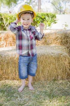 Cute Young Mixed Race Boy Laughing with Hard Hat Outside Near Hay Bale.