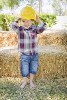 Cute Young Mixed Race Boy Laughing with Hard Hat Outside Near Hay Bale.