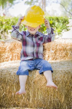 Cute Young Mixed Race Boy Laughing with Hard Hat Outside Sitting on Hay Bale.