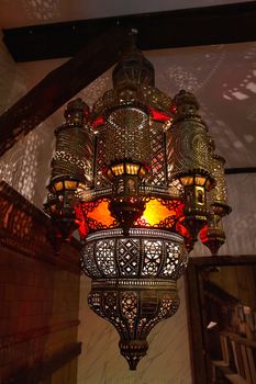 Typical handmade Moroccan Arabic lantern lamp illuminating patterns of light on the wall                               