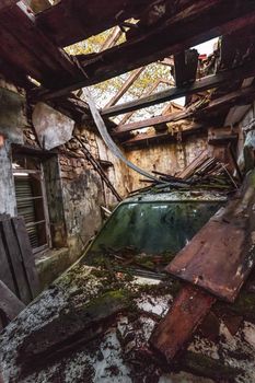 Damaged car in old wooden caban with broken roof