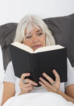 Mid age woman reading a nail-biting book in bed