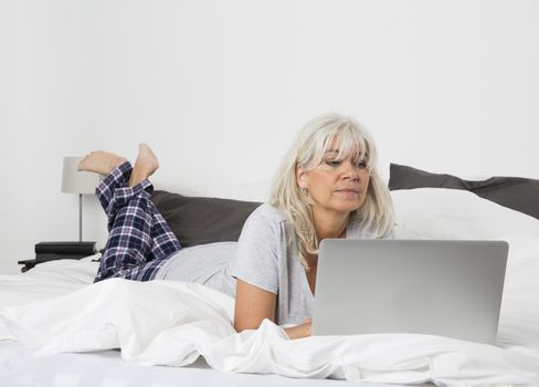 Mid age woman with a laptop lying down in bed