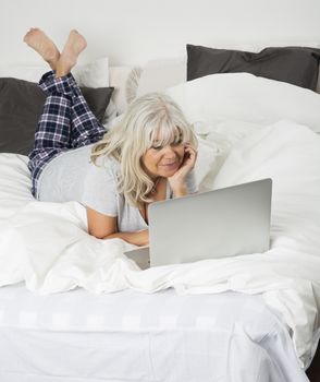 Mid age woman with a laptop lying down in bed, from high angle view