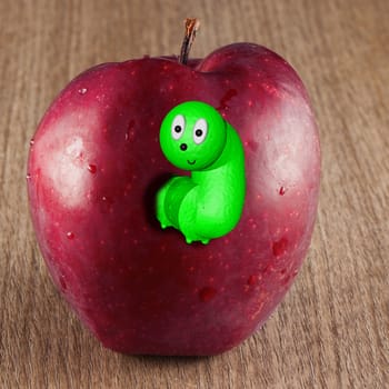 Toony worm coming out of a red apple over a wooden background