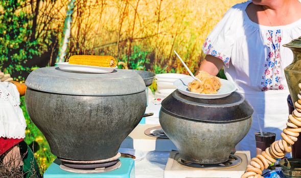 On the table are cooked in cast iron pots boiled corn, stewed potatoes, bagels, samovar to greet guests at the party under the open sky