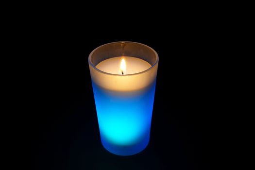 Photo of a burning light blue candle isolated on black background. Objects photography.