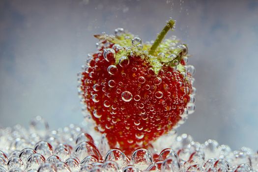 Photo of a strawberry with bubbles - underwater, on a blue background. Creative food photography.