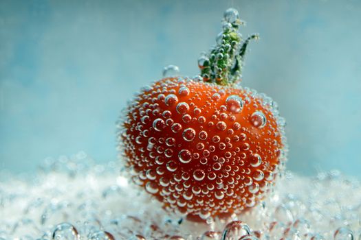 Photo of a cherry tomato with bubbles underwater on a blue background. Creative food photography.