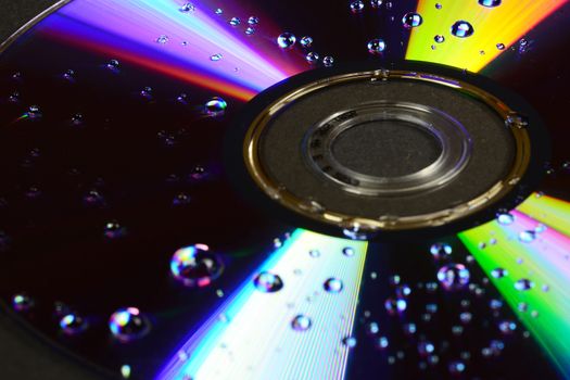 Photo of a compact disc with water drops isolated on black background. Objects photography.