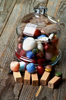 Various Colored Gum and Hard Candies in Glass Jar with Lid and Wooden Letters closeup on Rustic Wooden background