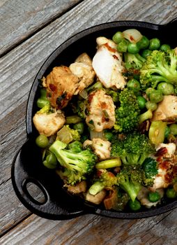 Chicken Stew with Broccoli, Bell Pepper and Green Pea in Black Saucepan isolated on Rustic Wooden background. Top View