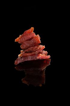 Beef jerky. Dry meat pieces isolated on black background. Delicious, culinary meat eating.