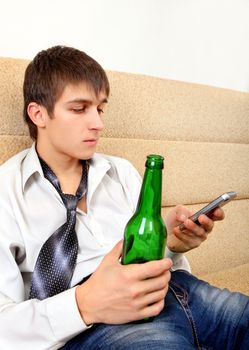 Teenager with Bottle of the Beer and Cellphone on the Sofa at the Home