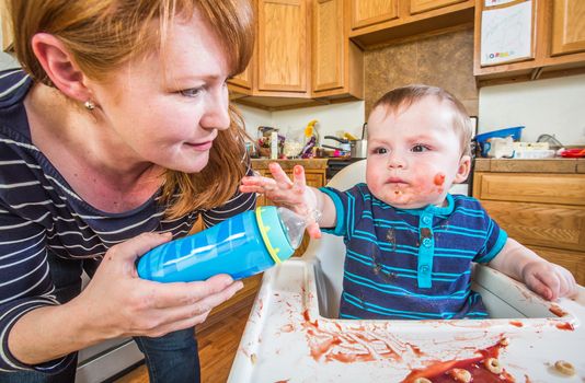 A woman in the kitchen feeds her baby from bottle