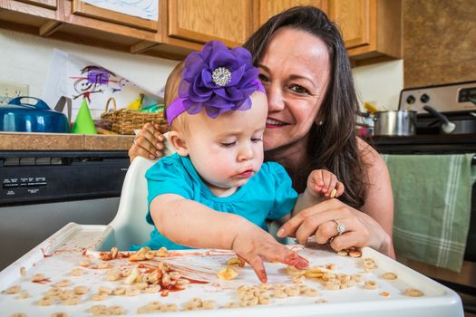 Mother in messy kitchen smiles as baby eats