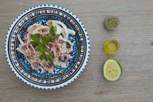 Marinated squid salad with fresh parsley in the traditional Tunisian plate. Oregano, olive oil and squeezed lemon close to the plate on the wooden surface. Free space for a text from the right side