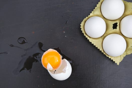Broken egg and four white chicken eggs on the black wooden surface. Top view. Background