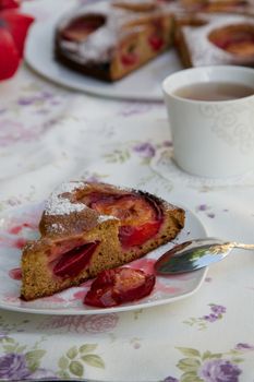 A piece of plum pie on a plate on the festive table. Plum pie and a cup of tea in the background