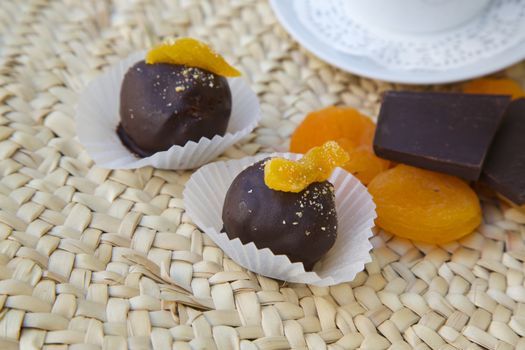 Handmade chocolate truffle with dried apricots on the woven surface. Dried apricots, pieces of black chocolate and a cup of coffee in the background