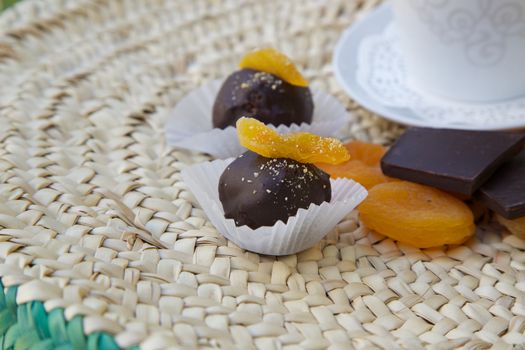 Handmade chocolate truffle with dried apricot on a woven surface. Dried apricots, pieces of chocolate  and a cup of tea in the background